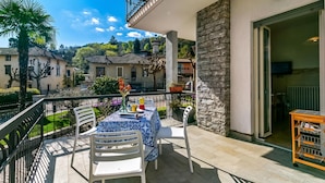A balcony with a table and chairs, a stone wall, and a view of surrounding buildings. - Il Giardino Di Dante Stresa Center: 2BR Terrace Apartment (Stresa)