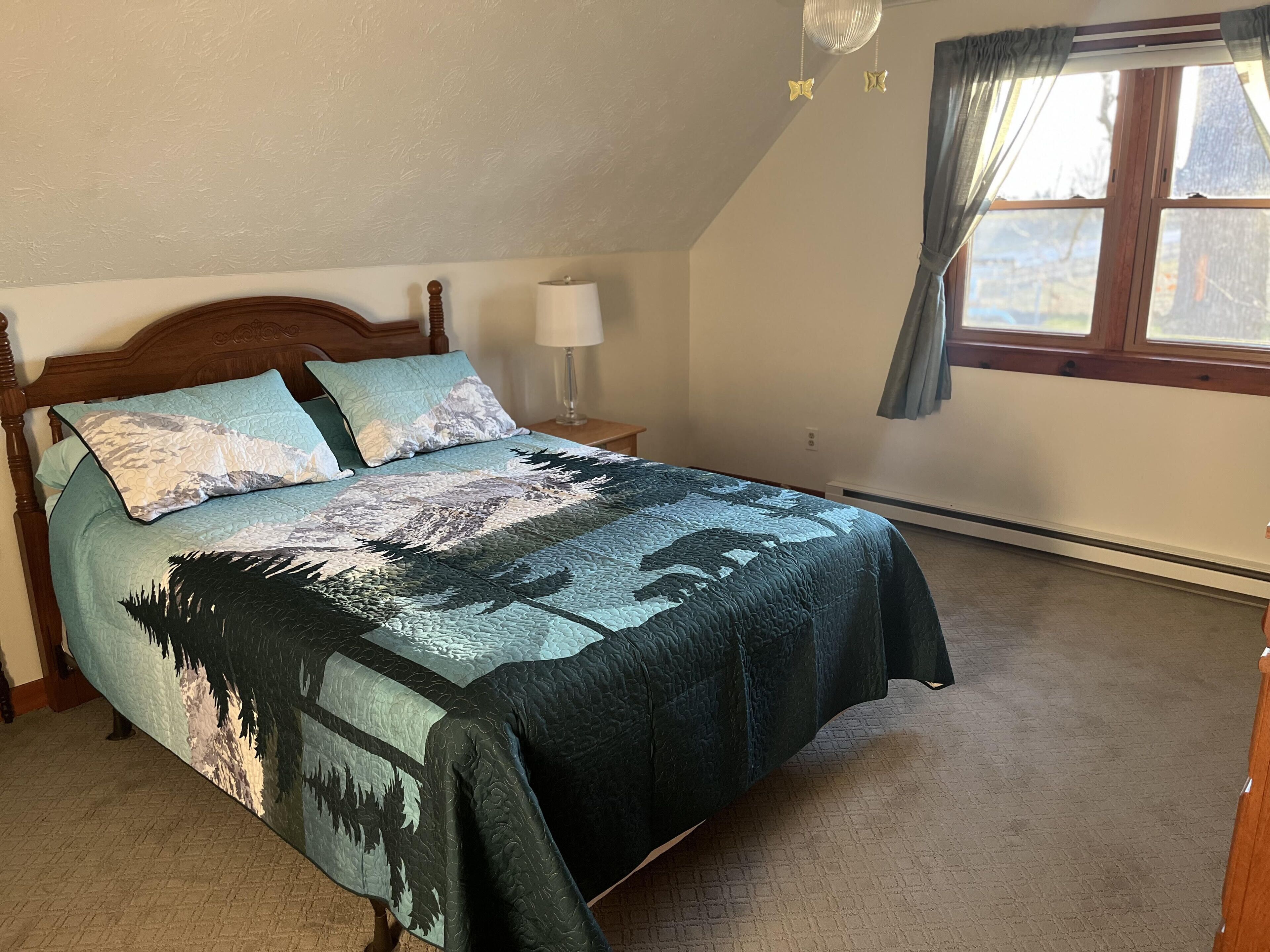 A bedroom with a bed, a nightstand, a lamp, a window with curtains, and a radiator.
