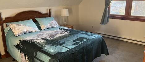 A bedroom with a bed, a nightstand, a lamp, a window with curtains, and a radiator.