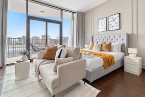 A modern bedroom with a large window, a sofa, a bed, and a nightstand.