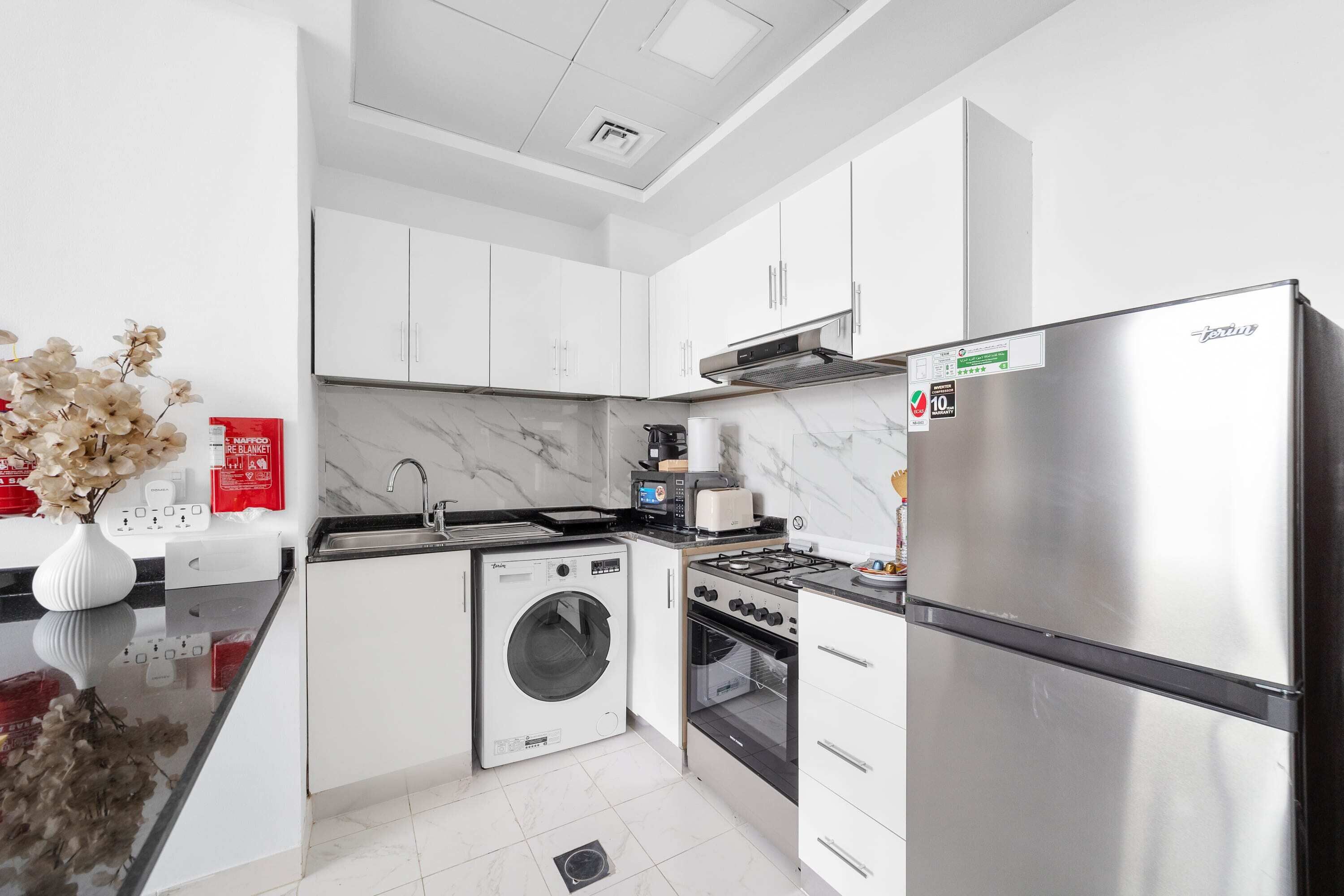 Une cuisine moderne avec des meubles blancs, un réfrigérateur en acier inoxydable, un lave-linge et une cuisinière.
