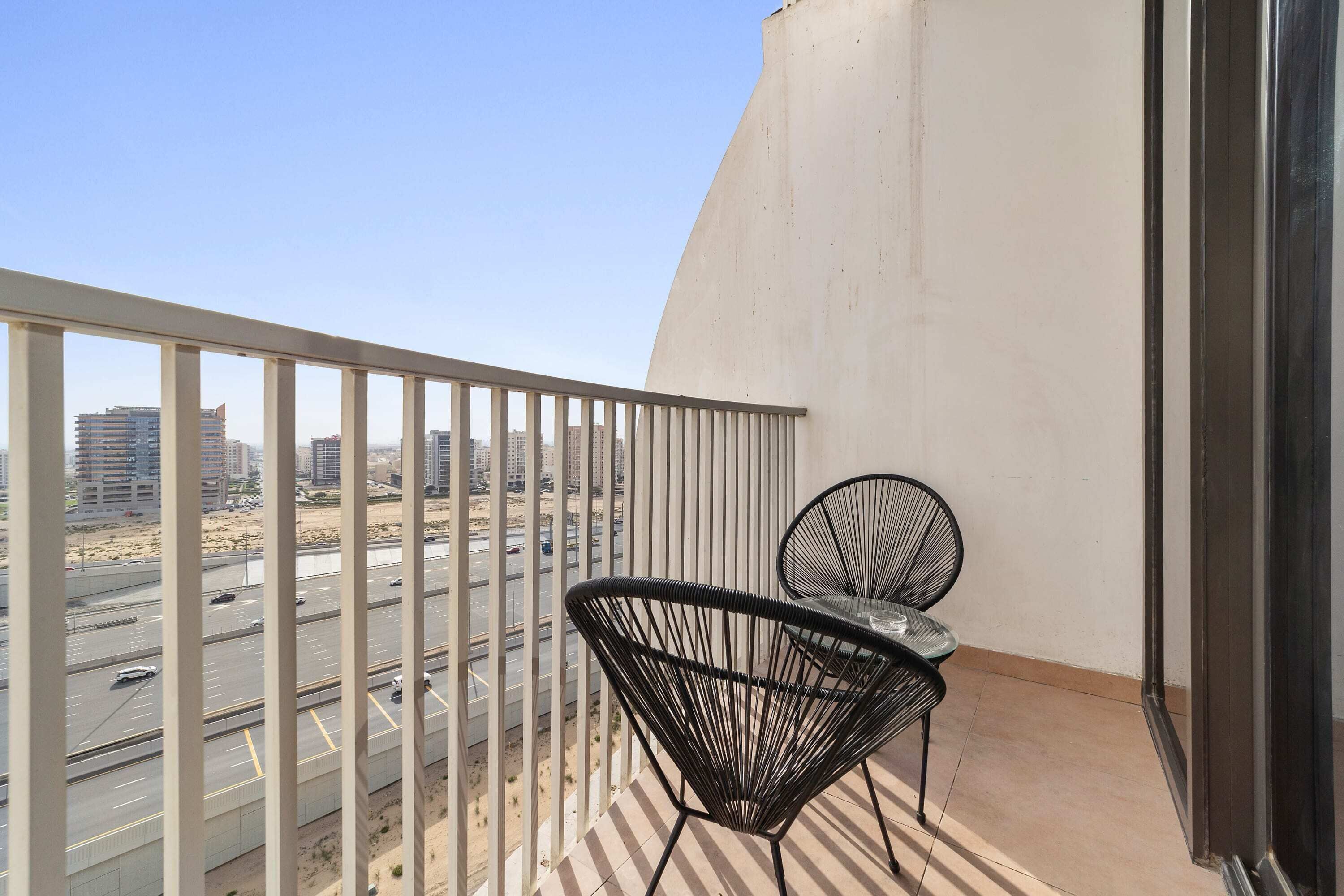 Un balcon avec une balustrade blanche, deux chaises noires et une table.