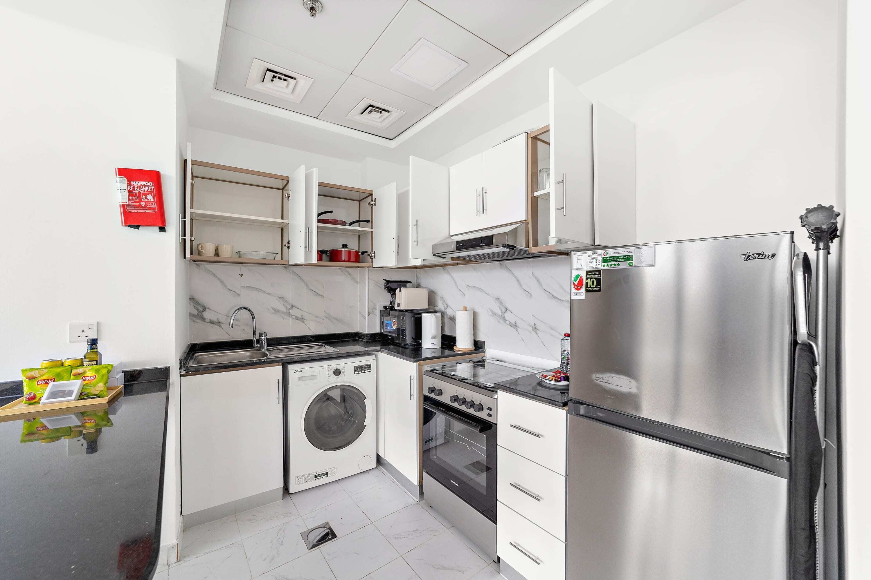 Una cucina moderna con mobili bianchi, un frigorifero in acciaio inossidabile, forno integrato e lavatrice.