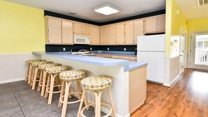 Une cuisine avec des meubles de rangement en bois, un réfrigérateur blanc, un four à micro-ondes et un coin bar avec des tabourets.