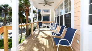 A wooden deck with blue chairs and a table, overlooking a street with palm trees. - 2nd Row 4 BR Beach House with a Private Pool! Peachy Pleasure   (Surfside Beach)