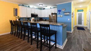 A kitchen with a central island, bar stools, and white cabinets. - 2nd Row 4 BR Beach House with a Private Pool! Peachy Pleasure   (Surfside Beach)