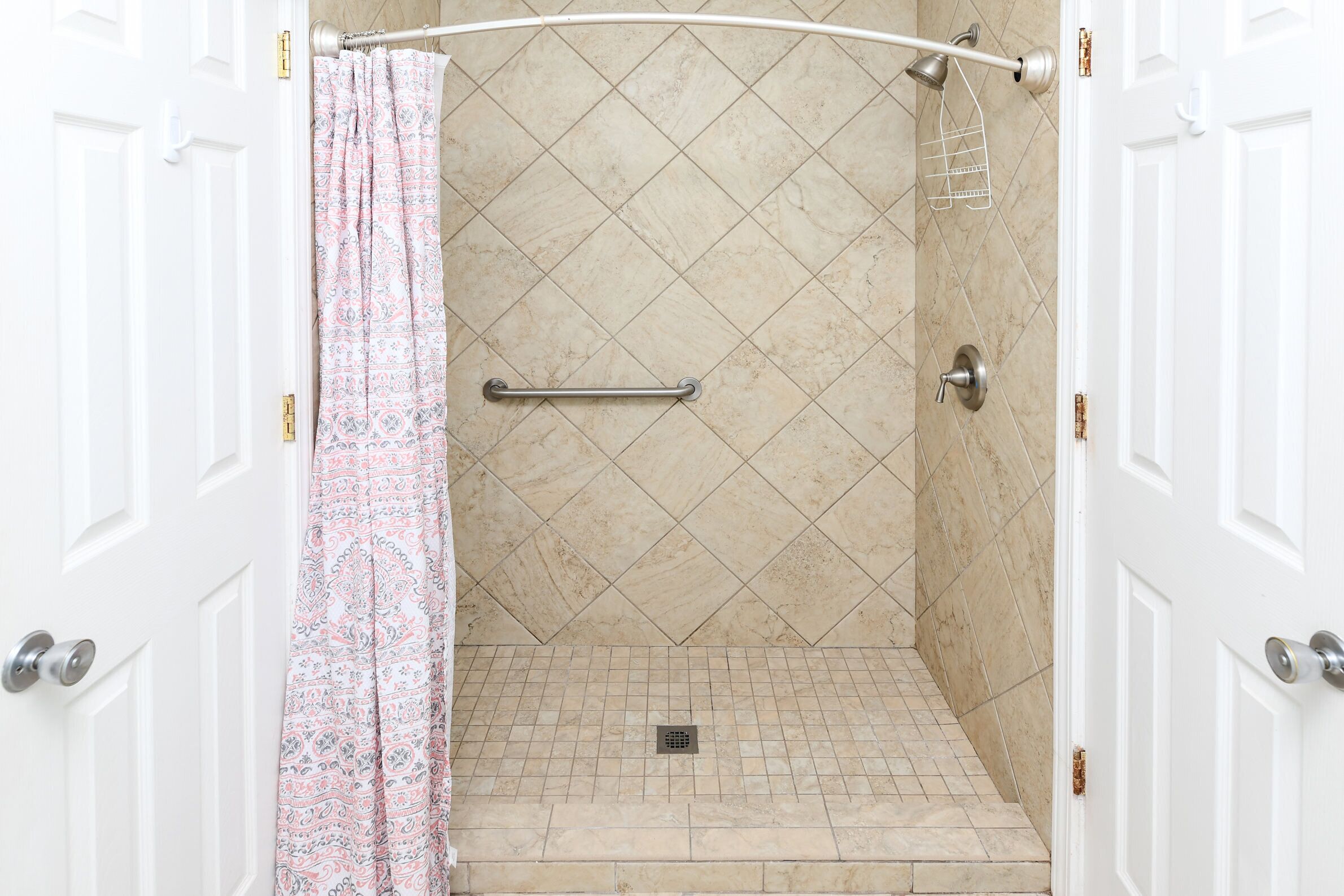 A walk-in shower with a shower curtain, a grab bar, and a tiled floor.