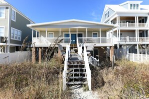 A two-story beachfront property with a covered front porch, a wooden staircase leading to the entrance, and a white fence surrounding the property. - Oceanfront 5 BR Beach House! Sam's Shack (Surfside Beach)