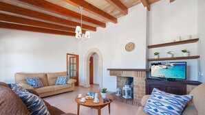 A living room with a sofa, armchairs, a coffee table with breakfast items, a fireplace, and a television displaying a beach scene. - Finca Vilar with pool, garden, 6 bedrooms, with A/C, 4 bathrooms, free Wifi (IB)