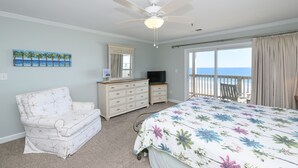 Un dormitorio con cama, una silla, cómoda, televisor y balcón con vista al océano.