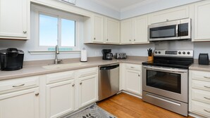 Una cocina moderna con armarios blancos, electrodomésticos de acero inoxidable, lavavajillas, cafetera y tostadora.