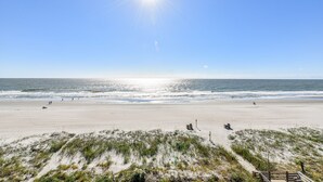 Una playa con cielo despejado, mar tranquilo y un paseo marítimo de madera que lleva al agua.