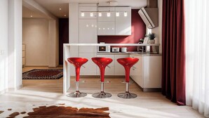 A modern kitchen with white cabinets, a red accent wall, and three red bar stools. - Qult·co - Old City Pearl (București)