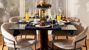 A dining table with a glass top, surrounded by upholstered chairs, set with plates, glasses, and a centerpiece. - Qult·co - Monarch (București)