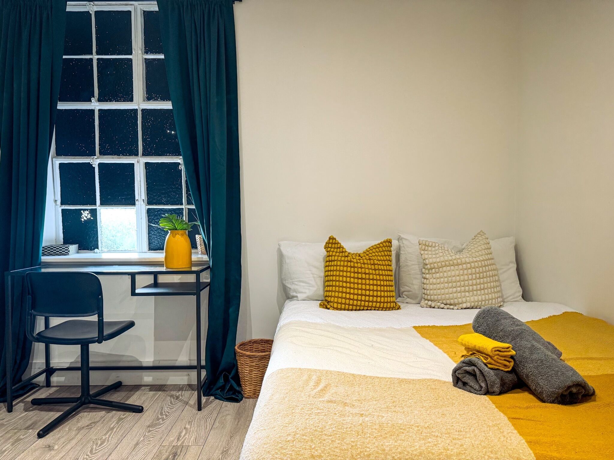 A bedroom with a bed, pillows, a desk, a chair, and a window with curtains.