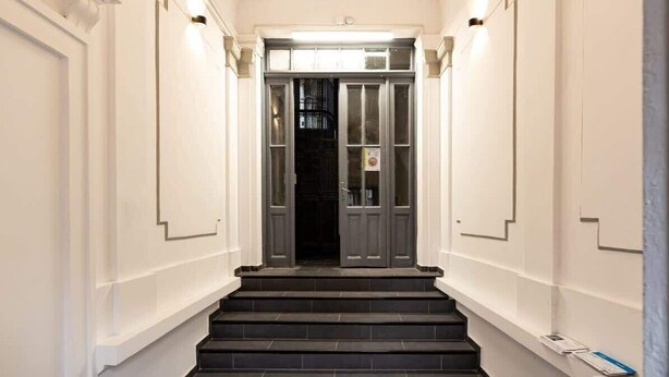 A staircase leading to a dark door with a light fixture above. - Qult·co - Misty Night (București)