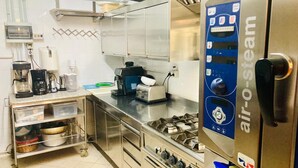 A commercial kitchen with stainless steel appliances, including an air-steam machine, coffee makers, and a gas stove.