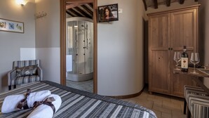 A hotel room with a bed, a wooden wardrobe, a shower, and a small table with wine glasses.