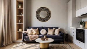 Una sala de estar moderna con un sofá azul oscuro, una mesa de centro redonda y un espejo decorativo en la pared.