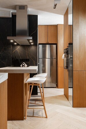 A modern kitchen with a marble backsplash, stainless steel appliances, wooden cabinets, and a white bar stool.