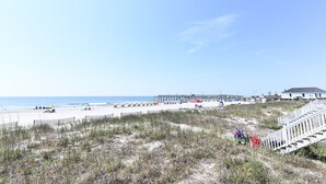 A beach with a wooden boardwalk, beach chairs, umbrellas, and a building in the background. - Oceanfront 4 BR Beach House with a Private Pool! Surfin' Turf (Surfside Beach)