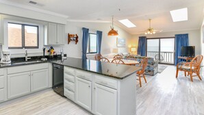 A spacious kitchen with a large island, a dining area with chairs, and a TV in the living room. - Oceanfront 3 BR Condo with a Shared Pool! Surfwatch III 401  (Surfside Beach)