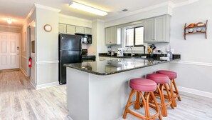 A modern kitchen with a central island, bar stools, and a refrigerator. - Oceanfront 3 BR Condo with a Shared Pool! Surfwatch III 401  (Surfside Beach)