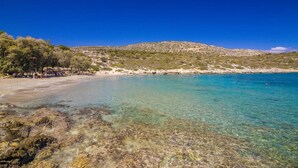 Ein Strand mit klarem türkisblauem Wasser, felsigem Ufer und einer hügeligen Landschaft im Hintergrund.
