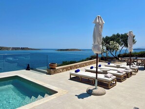 A poolside area with lounge chairs and umbrellas, overlooking a clear blue sea and distant land. - SeaWave Villa II with Heated Pool, By Hellocrete (Loutraki)