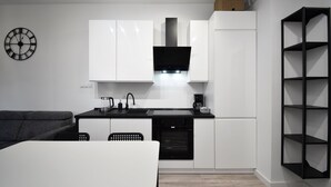 Una cocina moderna con armarios blancos, encimera negra y horno empotrado. Se ve una silla negra y una mesa blanca en primer plano.