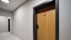 Pasillo con una puerta de madera marcada con el número 6, un interruptor de luz y un código QR en la puerta.