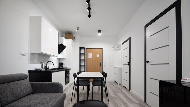Una cocina moderna con armarios blancos, una mesa de comedor con sillas, un sofá gris y una mesa redonda negra.