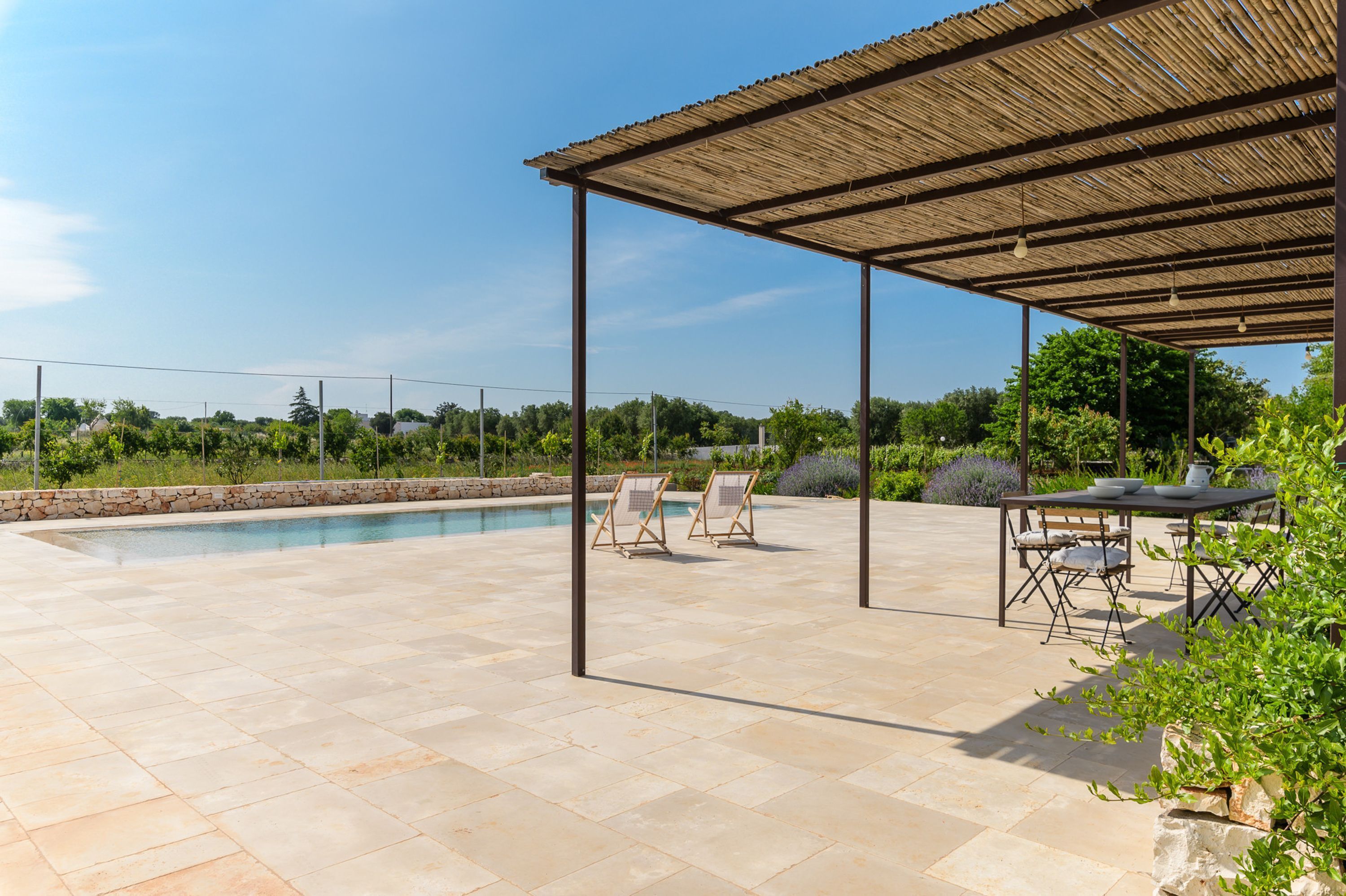A covered outdoor area with a pool, lounge chairs, and a table.