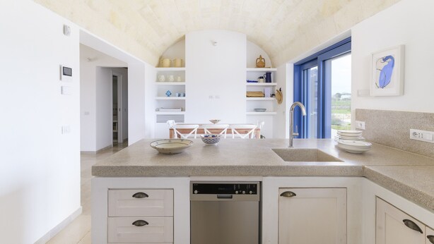A modern kitchen with a built-in dishwasher, white cabinetry, and a large window providing natural light. - Casa Blue con Piscina by Wonderful Italy (Ostuni)