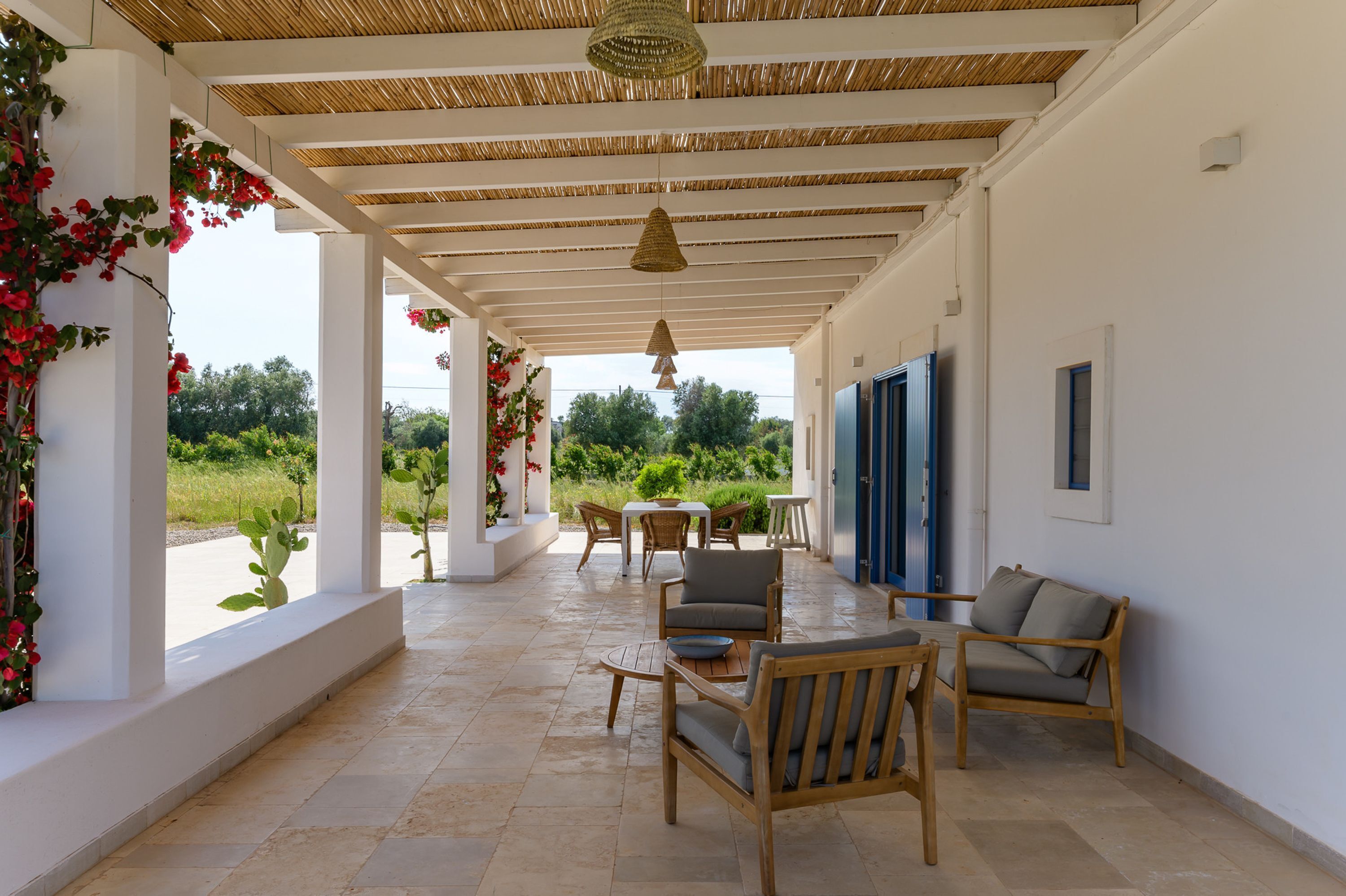 A covered outdoor area with a table and chairs, a hanging light fixture, and a view of greenery.