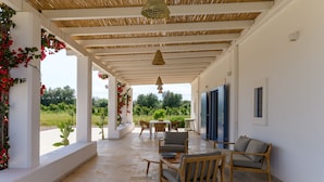 A covered outdoor area with a table and chairs, a hanging light fixture, and a view of greenery. - Casa Blue con Piscina by Wonderful Italy (Ostuni)