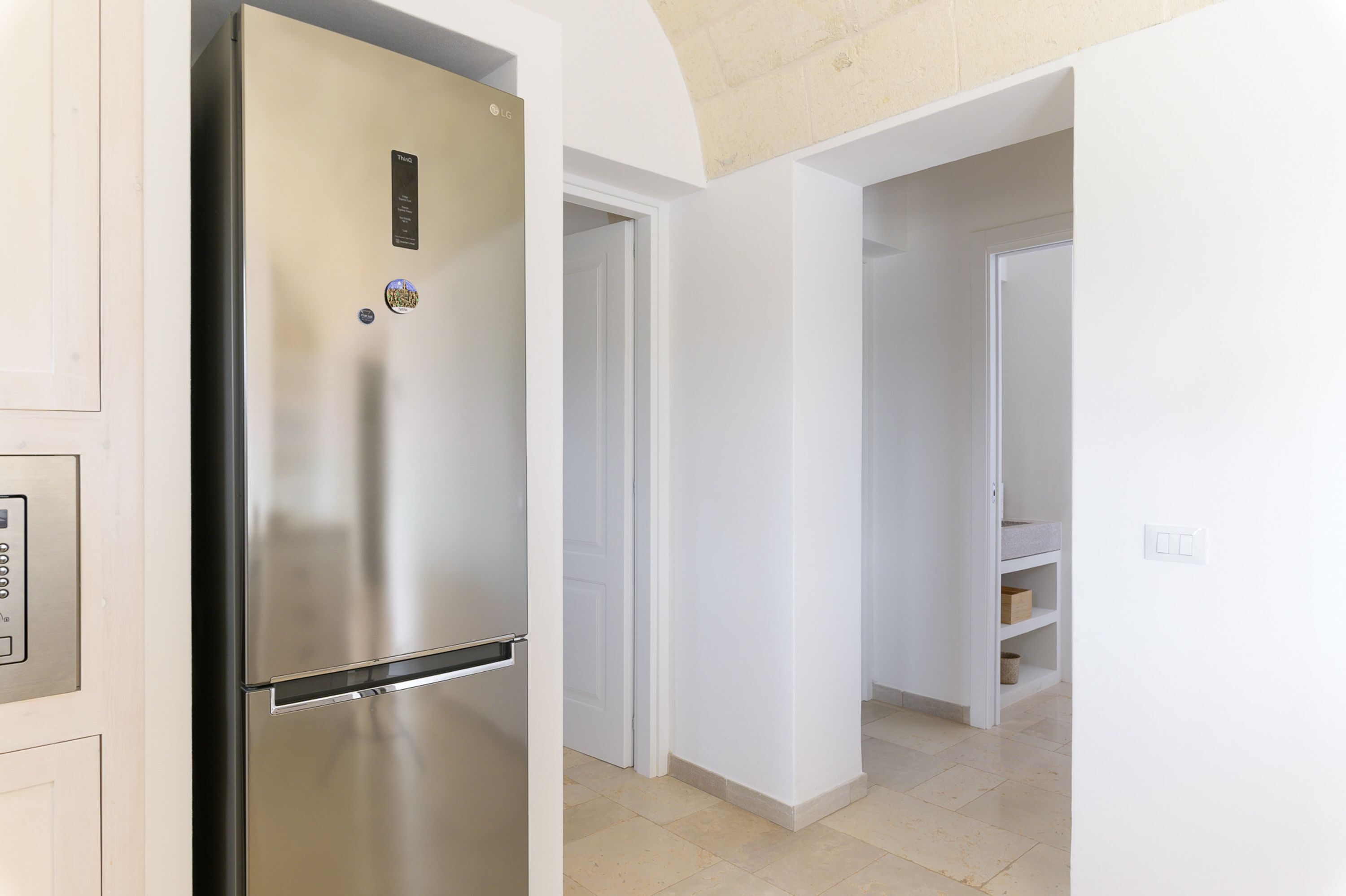 A modern kitchen with a stainless steel refrigerator, white walls, and a tiled floor.