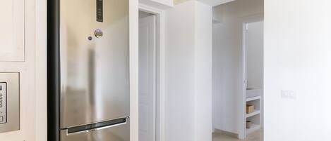 A modern kitchen with a stainless steel refrigerator, white walls, and a tiled floor.