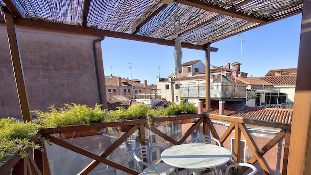 Un balcón acristalado con una mesa y sillas, con vistas a un paisaje urbano de edificios tradicionales.