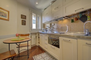 A kitchen with white cabinets, a wooden dining table with chairs, a window, and a tiled backsplash. - MOORS private terrace San-Marco (Venice)