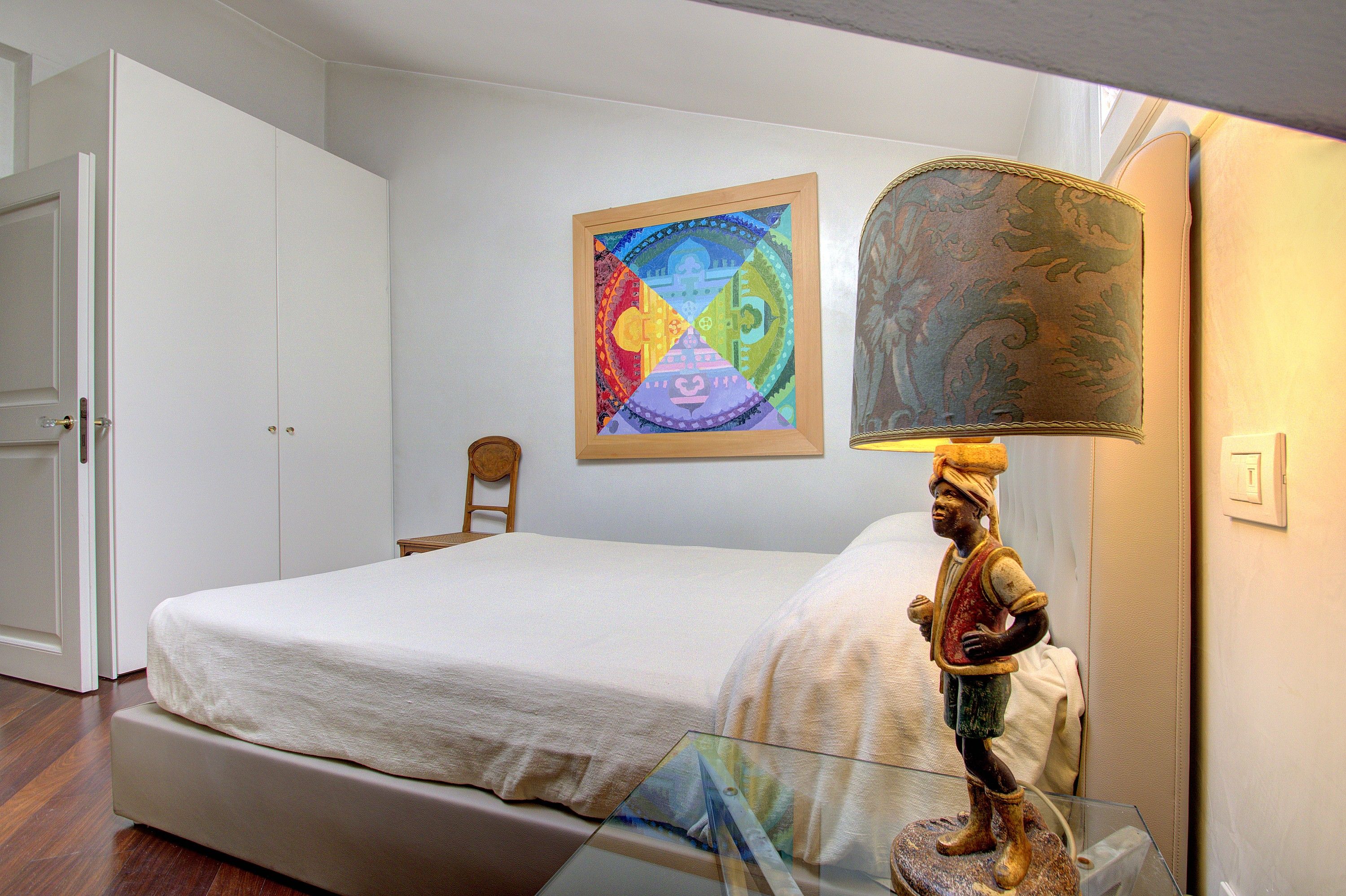 Ein Schlafzimmer mit einem Bett, einem Sessel, einer Lampe und einem Bild an der Wand.