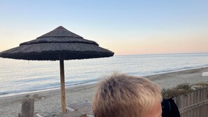 A wooden deck with a thatched umbrella, overlooking a beach with calm waters. - Animaux Interdits Parking Privé Proche de la mer vue mer (Santa Lucia di moriani)