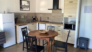 A modern kitchen with a dining table, chairs, a refrigerator, a dishwasher, a microwave, and a trash bin. - Animaux Interdits Parking Privé Proche de la mer vue mer (Santa Lucia di moriani)