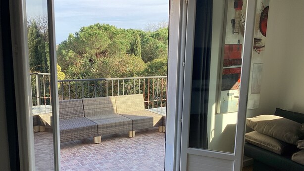 A room with a sliding glass door leading to a balcony with a wicker sofa and a metal railing. - Animaux Interdits Parking Privé Proche de la mer vue mer (Santa Lucia di moriani)