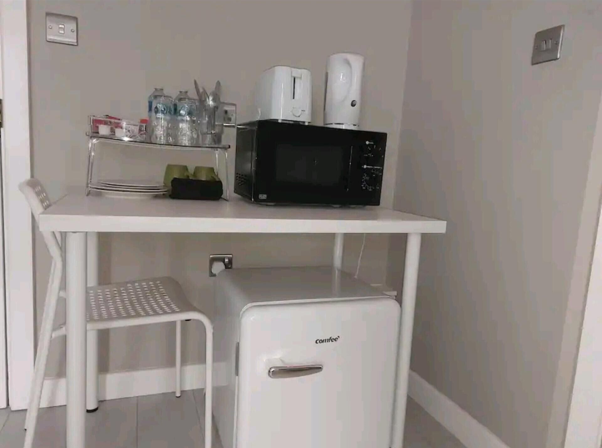 Eine Küchenzeile mit Mikrowelle, Kaffeemaschine und kleinem Kühlschrank.