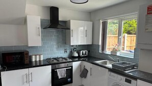 A modern kitchen with white cabinets, a black range hood, a microwave, a kettle, a toaster, a sink, and a washing machine.