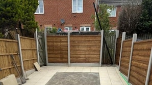 A backyard with a tiled floor, a wooden fence, and a brick house in the background.