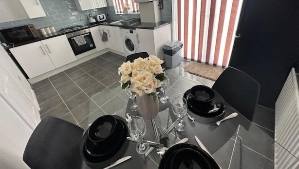 A modern kitchen with white cabinets, a black countertop, and a dining area set for four with a vase of flowers.