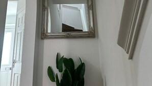 A hallway with a mirror, a plant, and a door.