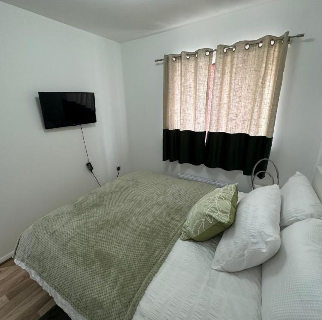 A simple room with a bed, a television mounted on the wall, and a window with curtains.